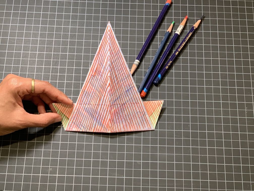 Colored pencils pictured alongside multi-colored triangle shaped paper