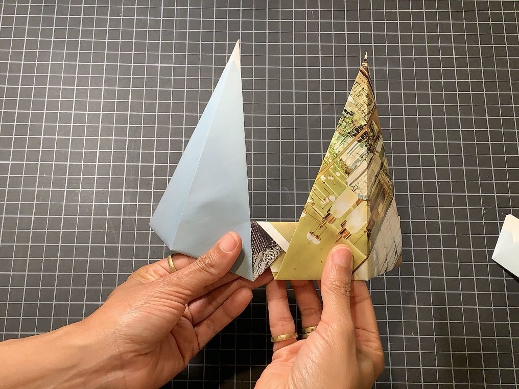 Two triangle shaped pieces of paper being connected at the bottom edges, held by two hands