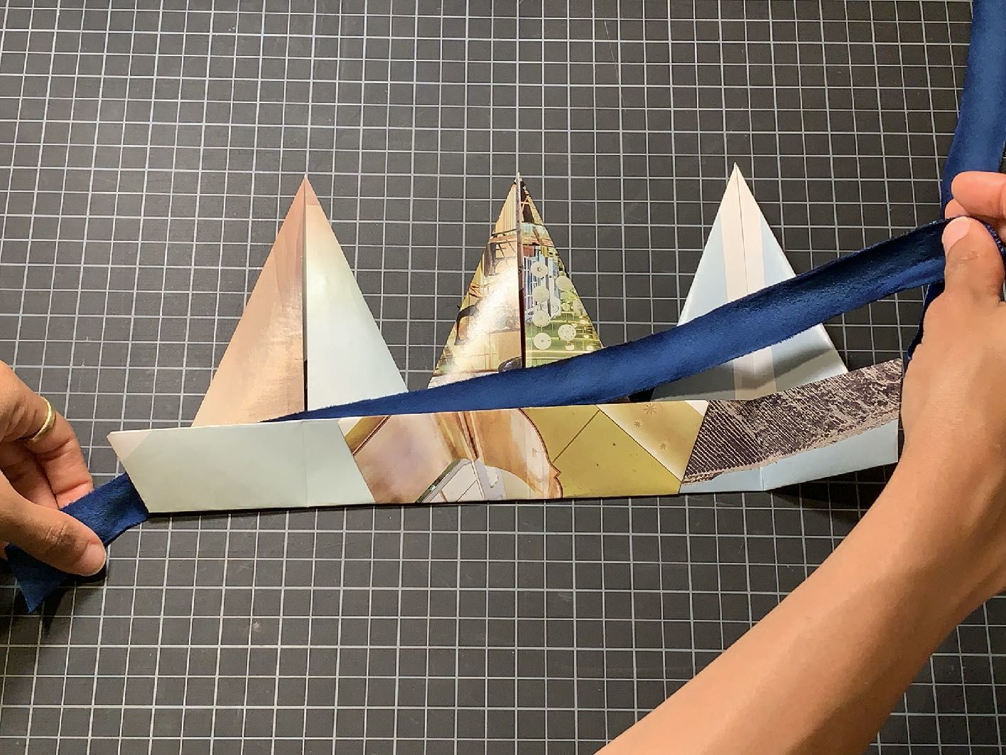 Blue ribbon being applied to the back bottom quarter of three attached triangle shaped pieces of paper