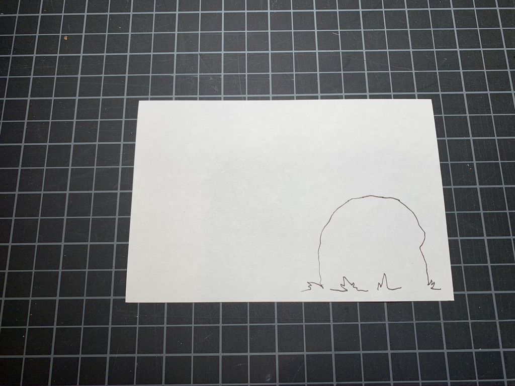 A drawing of a rock in black ink on a white card. Black and white grid in the background.