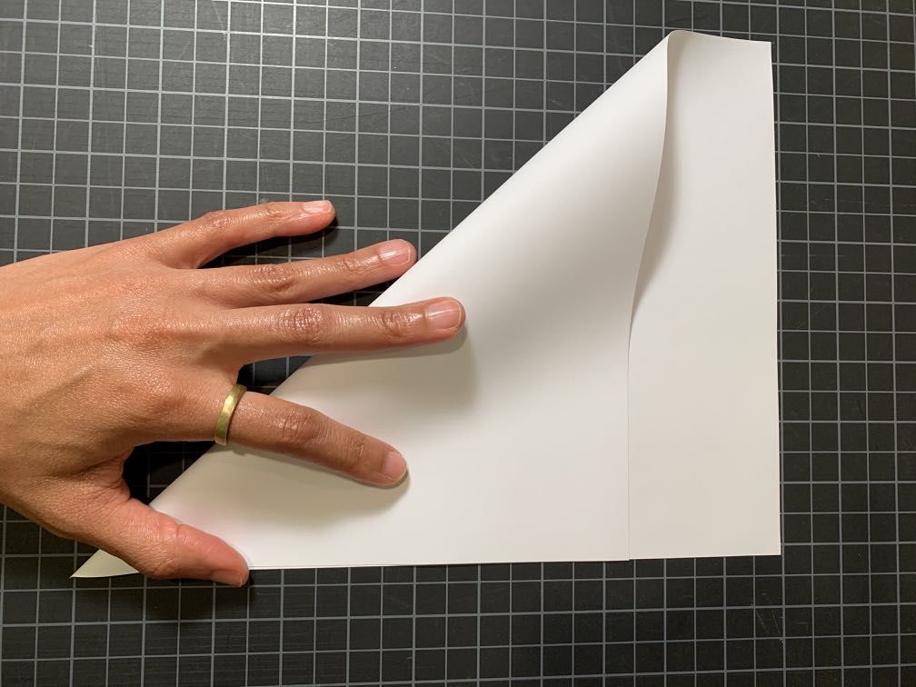 A hand folding a plain white piece of paper from upper left corner towards lower right