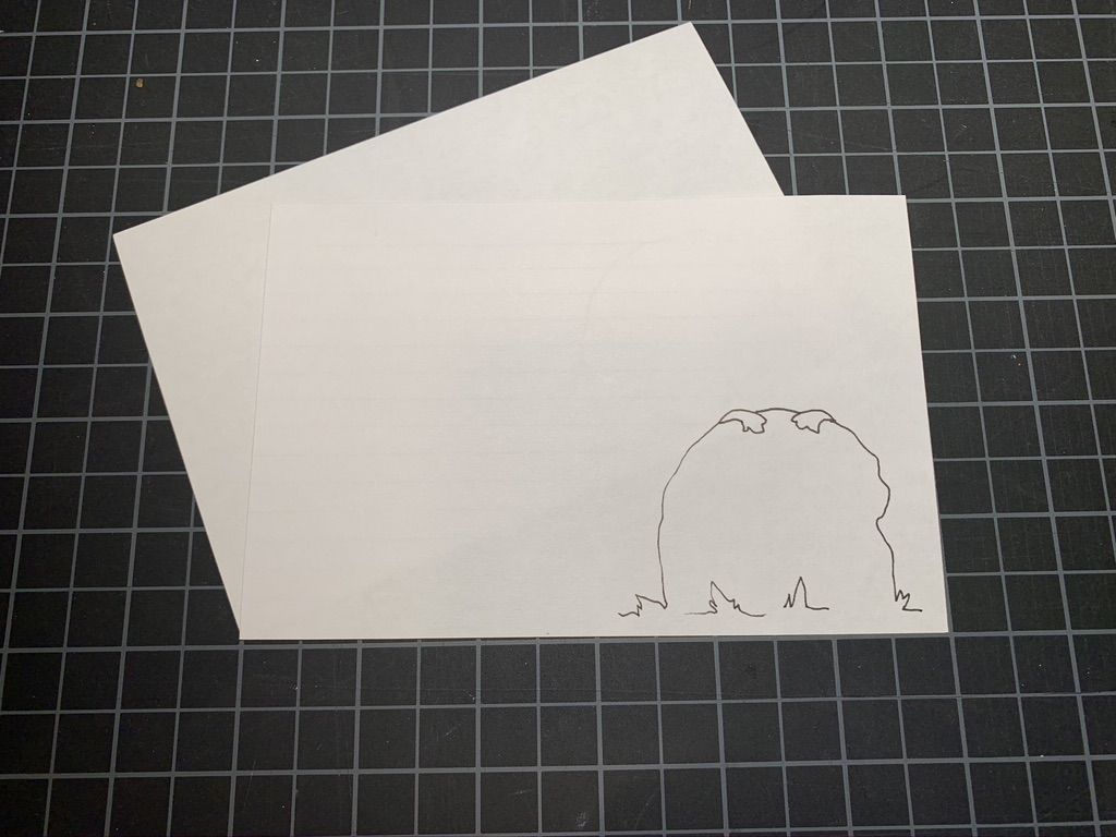 Pencil drawing of two paws on top of a rock on a white card. Black and white grid in the background.