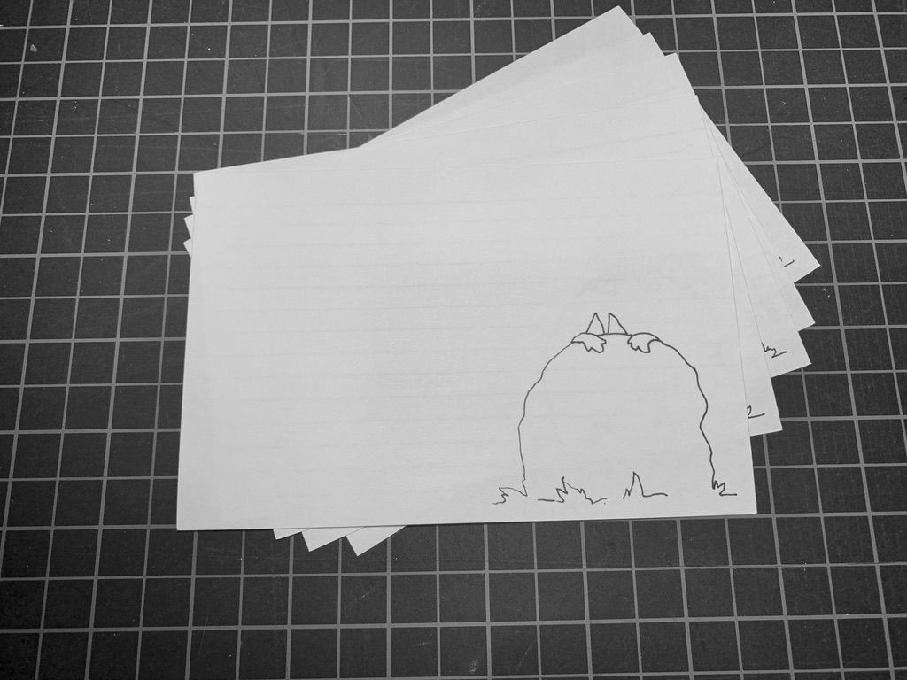 Pencil drawing of two paws on top of a rock with ears peeking out on a white card. Black and white grid in the background.