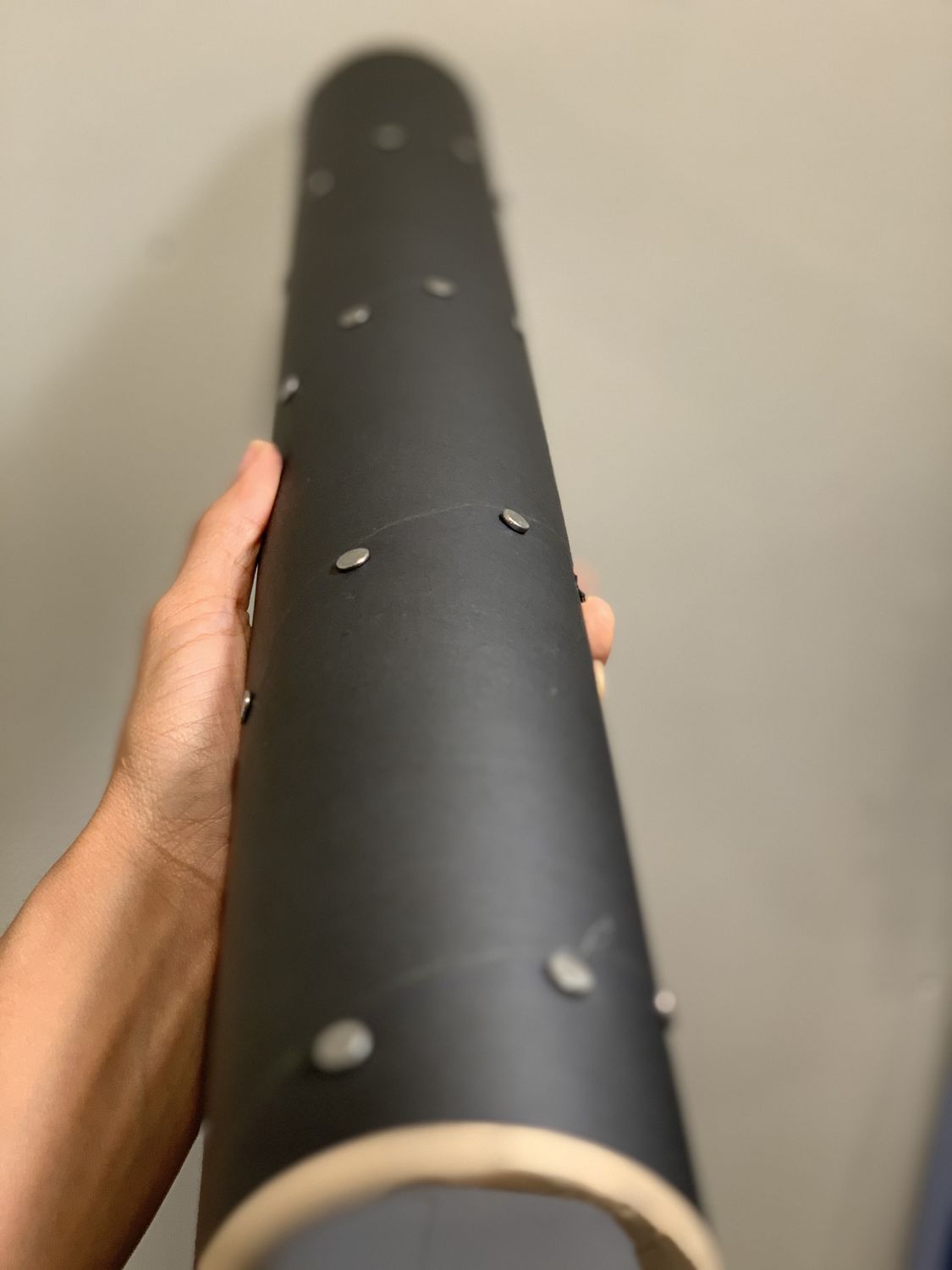 Close up image of black tube with silver nails inserted being held up against a gray background