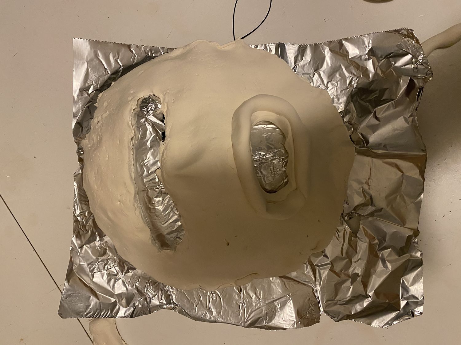 Clay mask with mouth and eye area hollowed out laid on top of piece of foil on flat surface