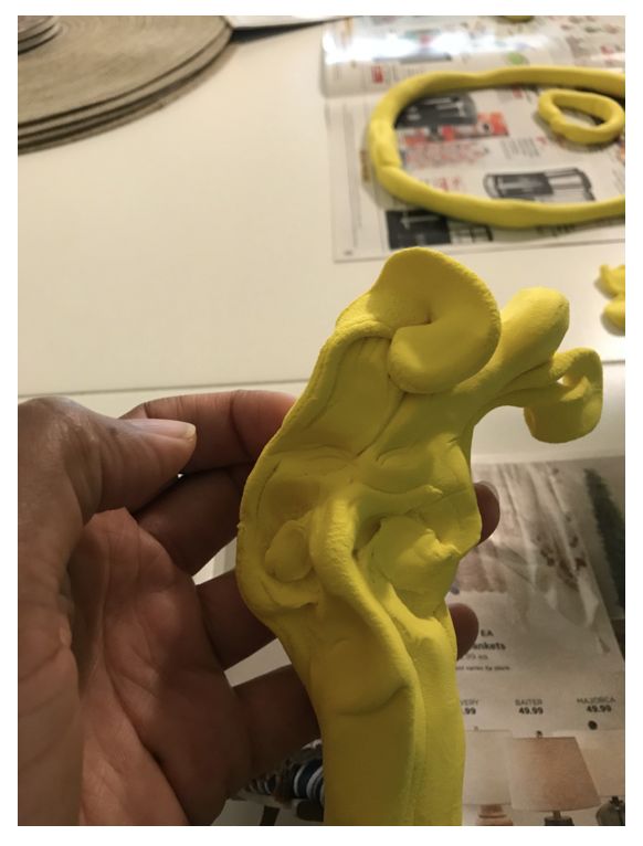 Yellow Model Magic sculpted in a curvy shape, held in someone's hand above an open magazine