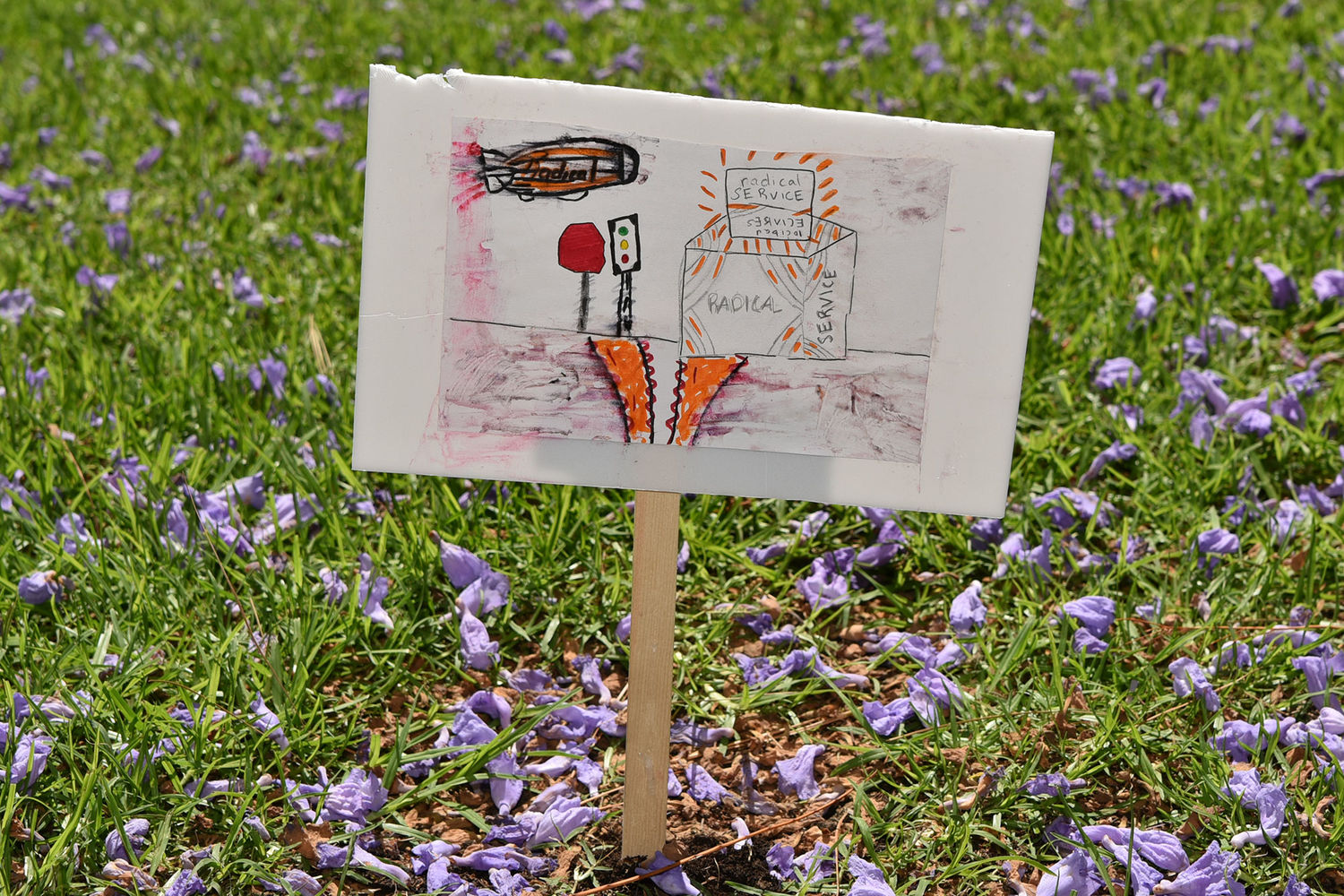 A small sign with an illustration on it is staked in the grass