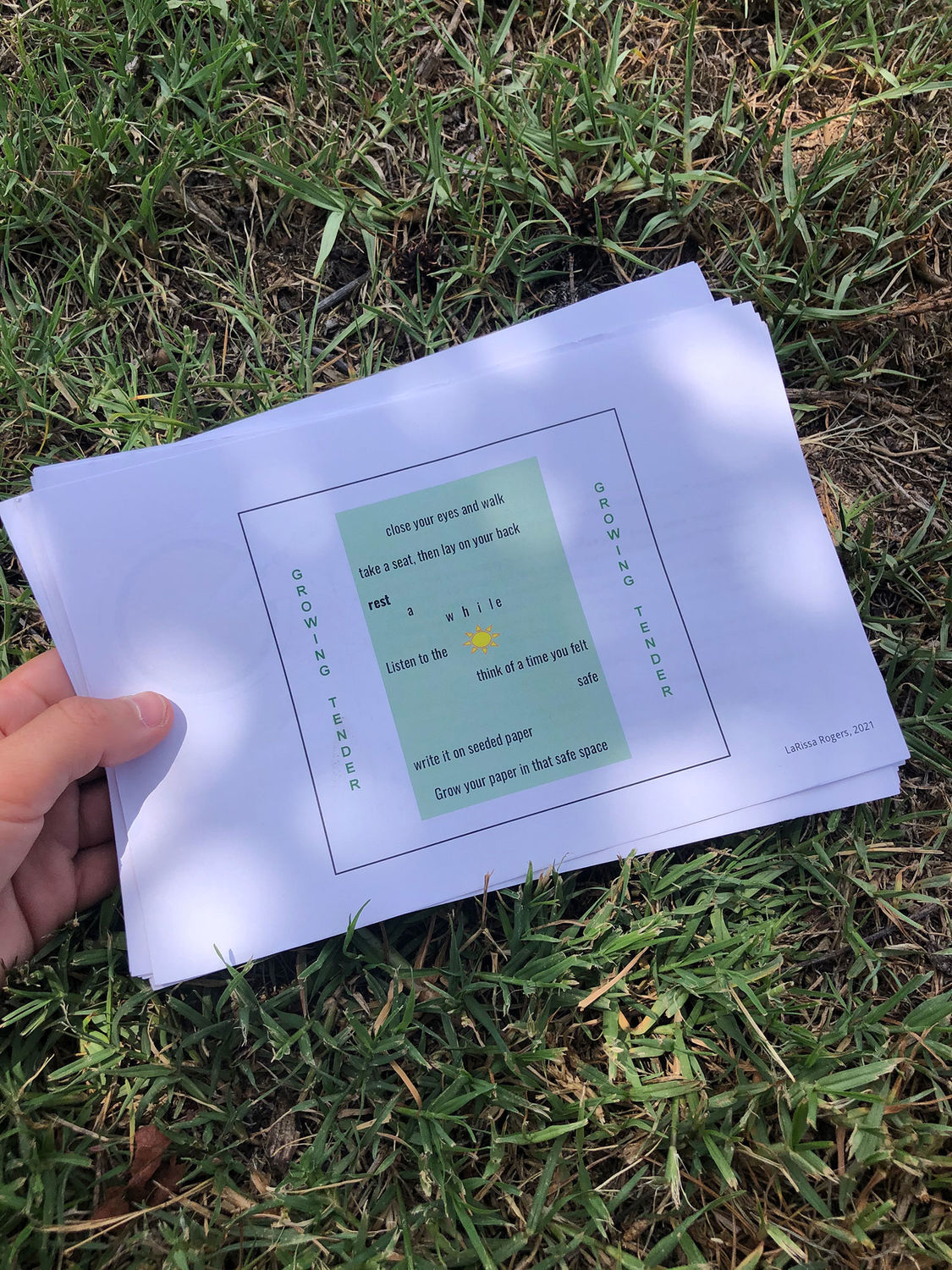 A hand holds a piece of paper against the grass. There are instructions written on the paper