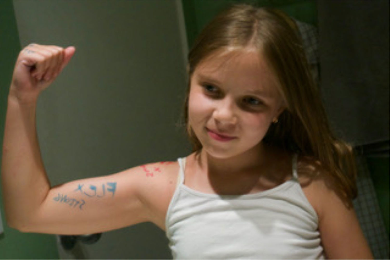 A young girl in a white top flexes her muscles