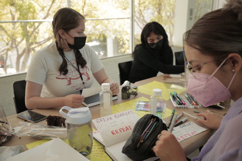 Three students in masks work at a table covered in brown paper