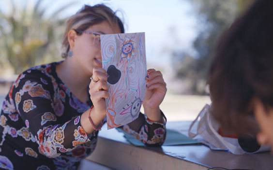 A woman holds up a colorful drawing on paper