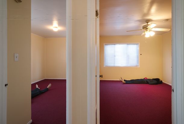 A view of an empty room with a maroon carpet and someone laying on the floor