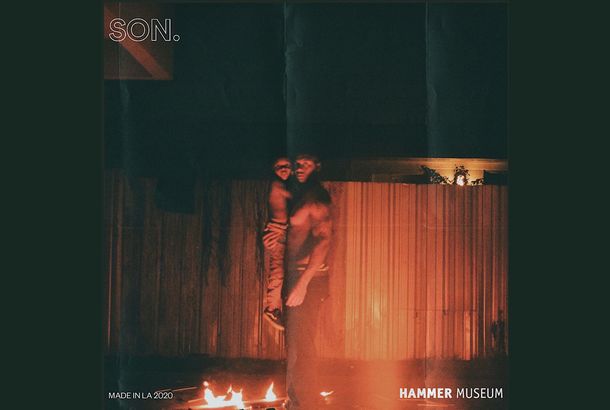 Dark photograph outside, at nighttime, of a man holding a small child, while standing in front of a fire in the foreground. The man is looking at the viewer, and the fire reflects against a fence in the background. Words are on the image: "SON." in the top left corner, "Made in L.A. 2020" in the lower left corner, and "Hammer Museum" in the lower right corner.