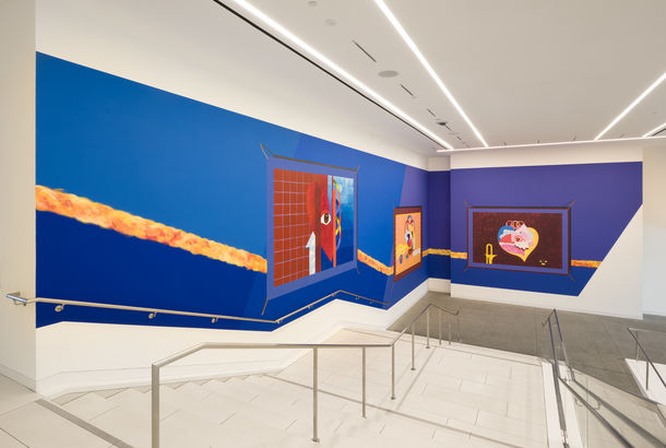 Mural on a bright blue background, installed along a large museum stairway