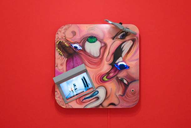 Square multi-media work with distorted images of faces and video screens, on a bright red wall