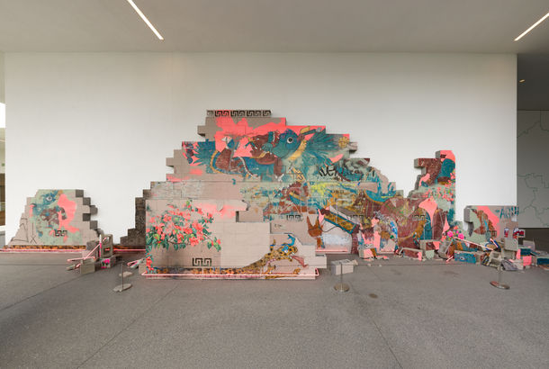 Installation featuring a crumbling wall of cinderblocks with handpainted images and pink neon lights