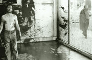 A man stands shirtless before a glass wall