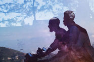 A silhouette of two people riding on a horse is set against a background of a dusk sky with shadows of trees.