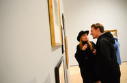 Two people look at paintings on a wall