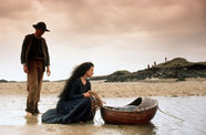 Still from the film The Secret of Roan Inish (1994) showing a woman crouching in the water, over a floating bassinet , with a man standing nearby