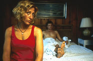 Still from the film Sunshine State (2002) showing a woman sitting in the foreground at the edge of a bed, and a man half-covered by a sheet sitting up against the headboard