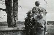 Two figures in masks stand before a stone wall