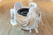 A sculpture of several white plastic chairs covered in a sheet, surrounding a tire