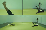 A rectangular image is divided into three segments. The bottom segment spans the full width  and depicts three figures wearing dark clothes in a room with a yellow floor. Two figures lie on the floor and the third stands against the back wall. On the upper left, an arm extends into the frame, with the hand lightly cupped. The image in the upper right shows an detail of the image at bottom, showing the two figures on the right end of that image.