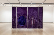 A large gallery with white walls. In the center of the room a large square structure of white poles and purple fabric covering the surface. On the  side of the structure there is a large hole, which provides a view of the inside.