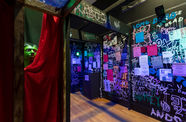 A green head pokes out from behind a red curtain in a flyer- and graffiti-covered haunted house