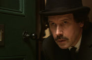 Still from the film "Bloom" (2003) showing actor Stephen Rea portraying the character Bloom, wearing a black bowler hat and peering through a doorway.