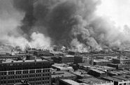 Black and white aerial photo of huge billows of smoke rising from Tulsa, Oklahoma, as it burned from the result of the 1921 Tulsa Race Massacre.