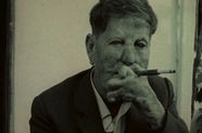Still from the film 1972 film "L'Ordre," showing a man with leprosy  in a suit smoking a cigarette..