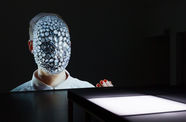 A figure with a jeweled face on a screen before a white platform