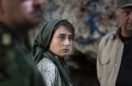 A woman wearing a hijab staring, located between two blurred men. 