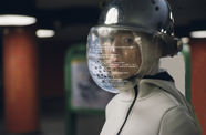 A woman wears a helmet with a plastic face shield. Formulaic text covers the face shield.