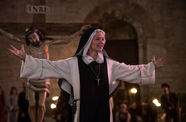 Still from the film "Benedetta" (2021), showing a nun with outstretched arms in front of a triumphal cross