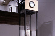 A large rock hung by a wire inside a clear glass box with a clock