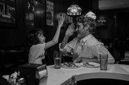 A man and a child sit at a table in a restaurant, giving each other a high five.