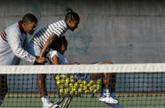 A man and a woman push a girl who sits inside of a shopping cart filled with tennis balls.