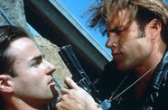 A man holds a gun in front of another man's face. 