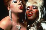 Two women wearing heavy makeup make kissing expressions. 