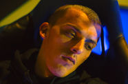 Still from the film "Atlantide" (2021), a closeup of a young man reclining in a chair, bathed in glowing blue light