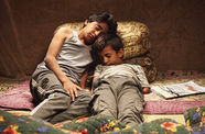 Two young boys lie together on several textiles and pillows. 