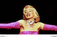 Marilyn Monroe with her arms spread out wearing a silky pink dress. 