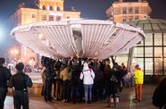 Several people attempt to touch a tall trumpeting structure in the center of a fountain.