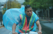 Man wearing poncho bikes in rain. 
