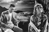 Man and a woman sit in front of an ocean background. 
