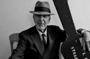 Black and white photo of musician Leonard Cohen seated with his arm around a guitar case