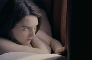 A woman lies on a bed and looks out a window. 